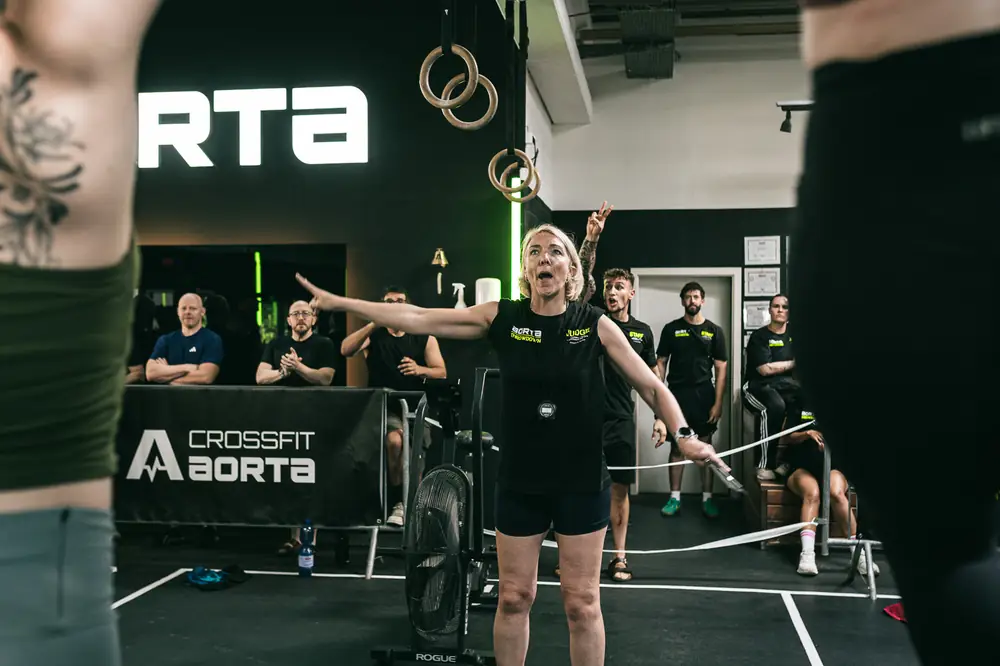 Athletin breitet beim Finish die Arme aus, Zuschauer am Wettkampfbereich des Aorta Throwdown in Berlin