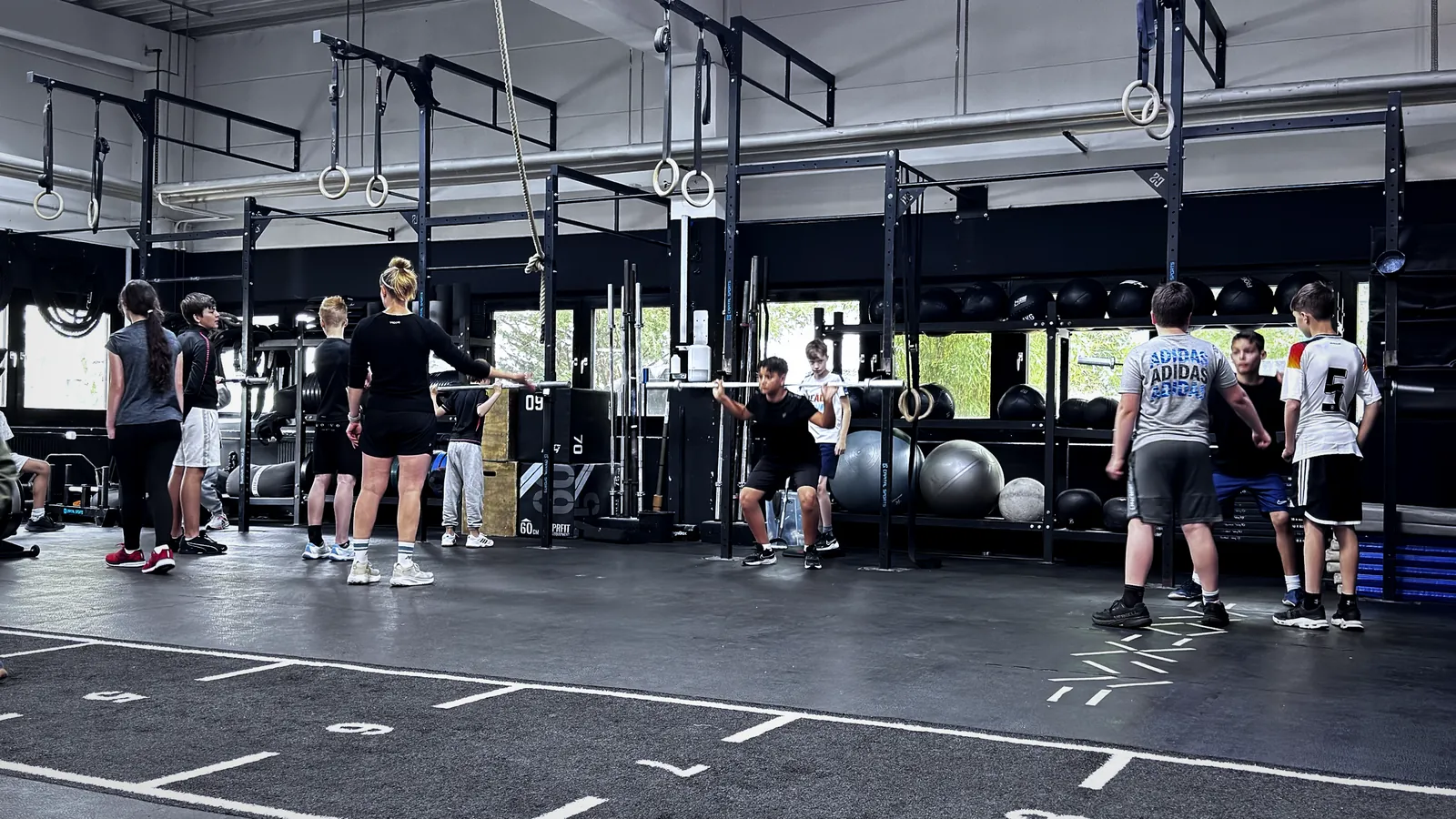 Coach korrigiert die Technik einer Kniebeuge mit Langhantel beim CrossFit Teens Training in Berlin-Tempelhof