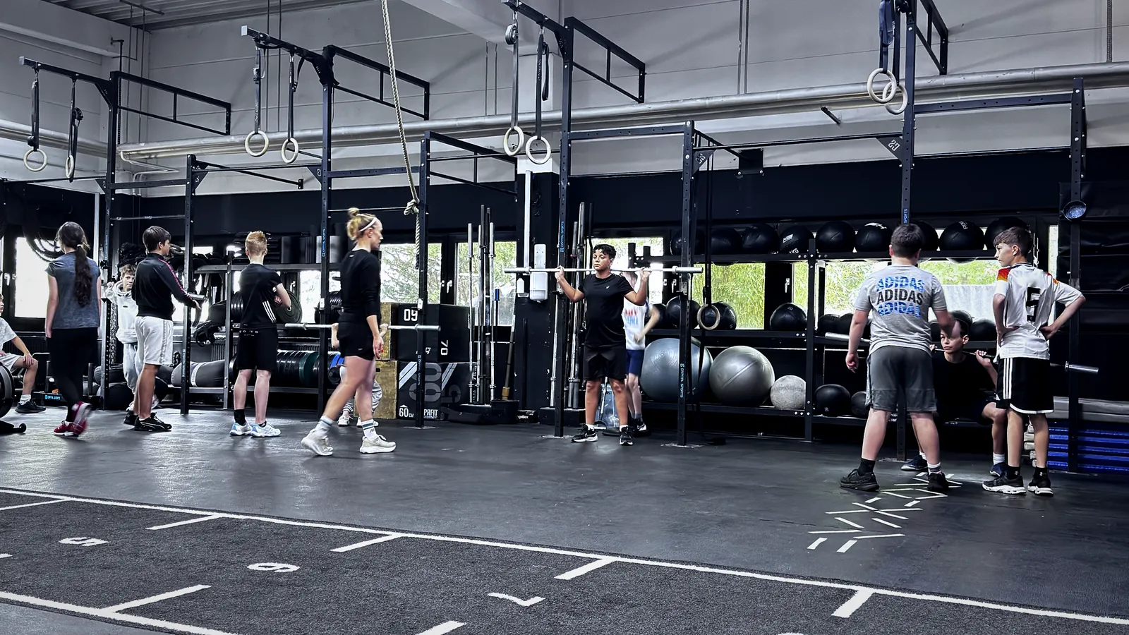 Jugendliche trainieren mit Langhantel, der Coach beobachtet die Gruppe beim CrossFit Teens Training bei Hyrox & CrossFit Gym Aorta in Berlin-Tempelhof