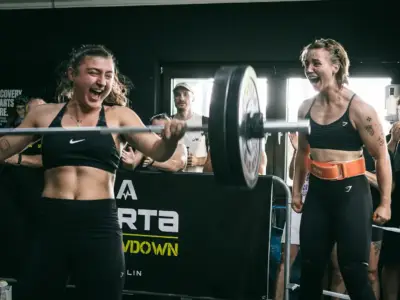 Athletin mit der Langhantel im Front Rack beim Aorta Throwdown in Berlin, ihre Teampartnerin feuert sie an