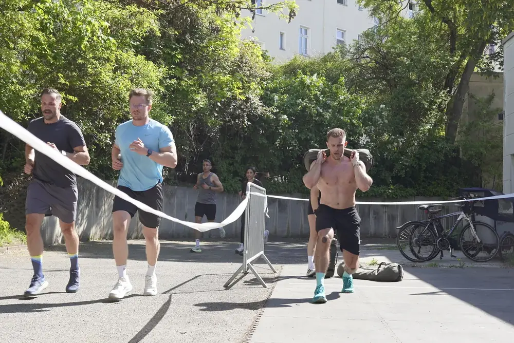 Sandbag Lunges und Läufer im Ziel bei der HYROX Simulation in Berlin